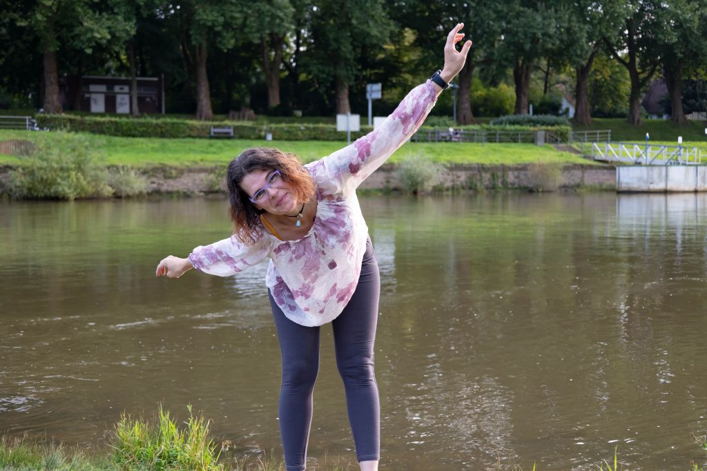 Frau mit ausgebreiteten Armen vor einem See